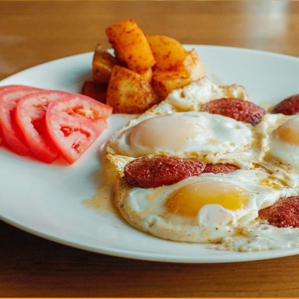 Turkish breakfast plate with fried eggs, sucuk sausage, roasted potatoes, and sliced tomatoes.