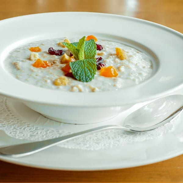 Turkish breakfast bowl with oatmeal, dried fruits, nuts, and mint, served with a spoon.