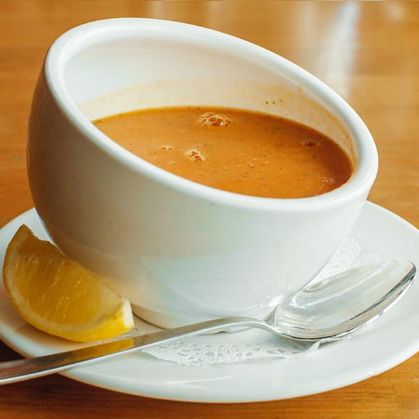 A white bowl of Turkish lentil soup with a lemon wedge and spoon on a white saucer.