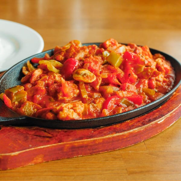 Turkish chicken saute with red and green peppers in a cast iron skillet on a wooden board.