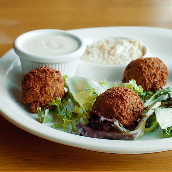 Three falafel balls on a bed of lettuce with two dipping sauces on a white plate.