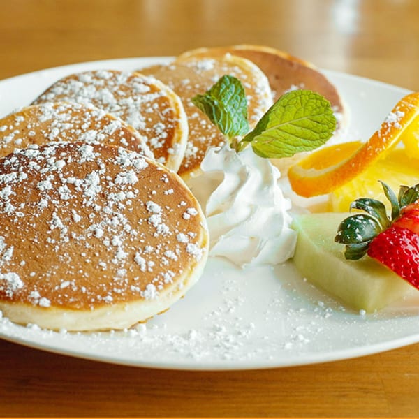 Fluffy pancakes dusted with powdered sugar, served with whipped cream, mint, and fresh fruit.