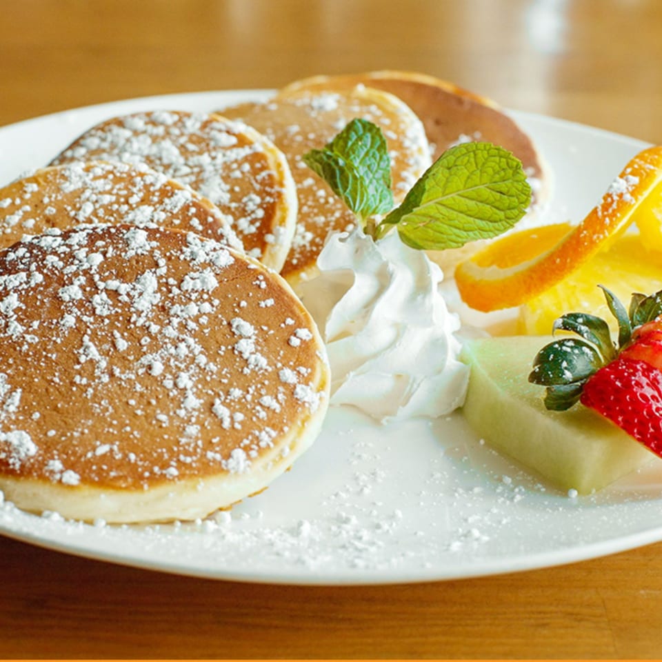 Fluffy pancakes dusted with powdered sugar, served with whipped cream, mint, and fresh fruit.