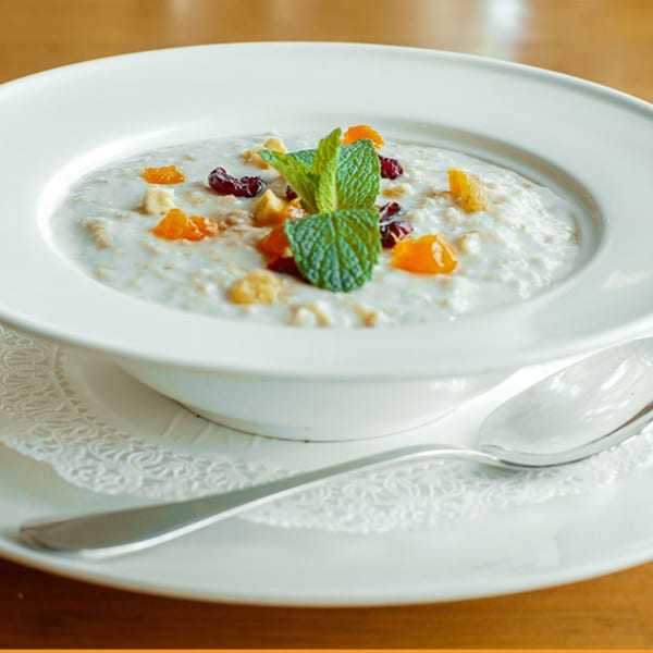 Creamy Turkish oatmeal topped with dried apricots, cranberries, nuts, and fresh mint in a white bowl.