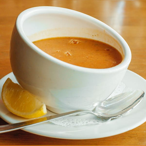A white bowl of Turkish lentil soup with a lemon wedge and spoon on a white saucer.