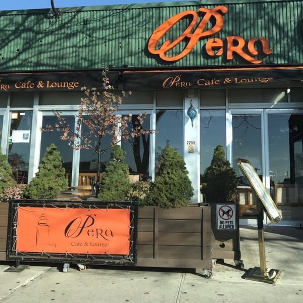 The exterior of Opera Cafe Lounge, a Turkish restaurant, with its orange sign and outdoor planters.