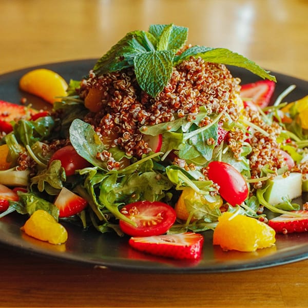 A vibrant quinoa salad with arugula, strawberries, cherry tomatoes, and orange segments, garnished with mint.