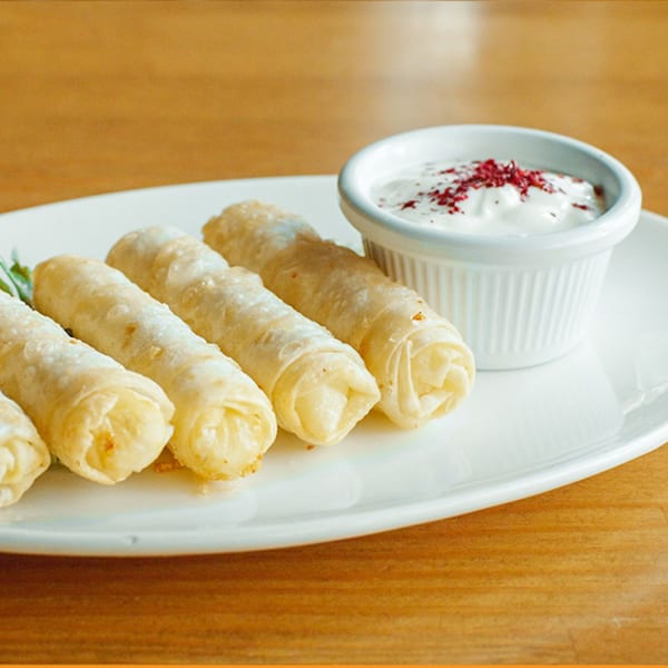 Turkish sigara boregi, fried pastry rolls, on a white plate with a side of yogurt dip.