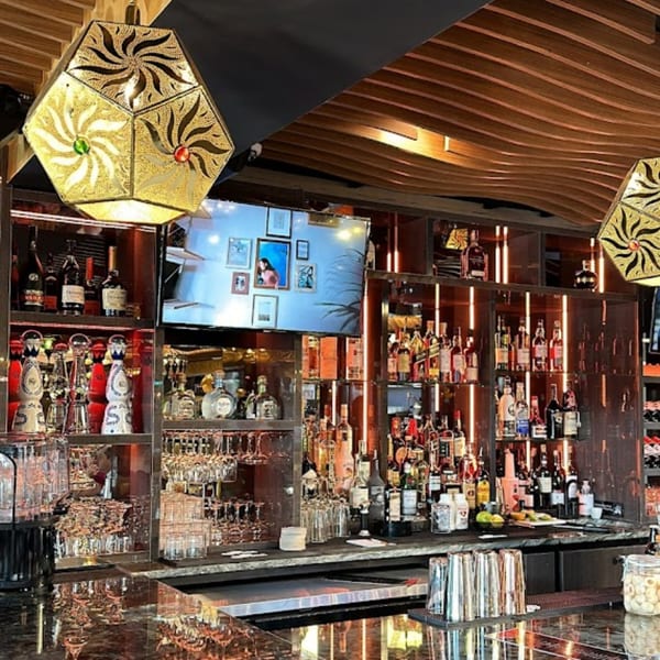 A well-stocked bar at Opera Cafe Lounge with bottles, glasses, and decorative Turkish lamps.