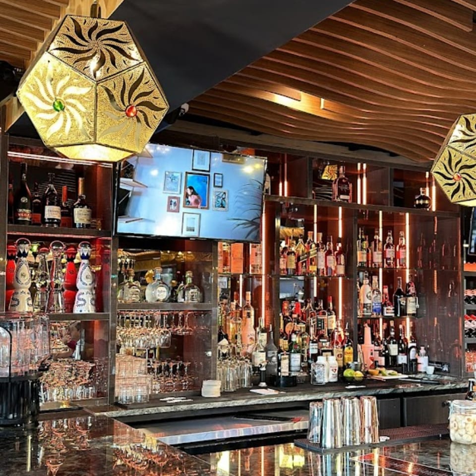 A well-stocked bar at Opera Cafe Lounge with bottles, glasses, and decorative Turkish lamps.