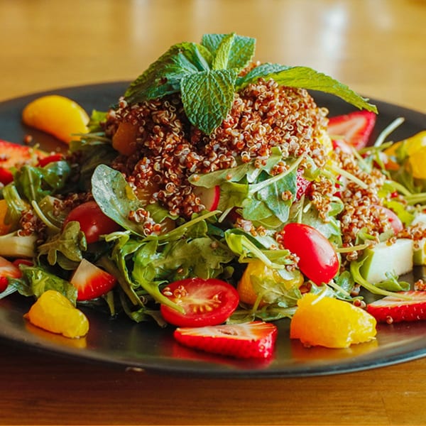 A vibrant quinoa salad with arugula, strawberries, cherry tomatoes, and orange segments, garnished with mint.