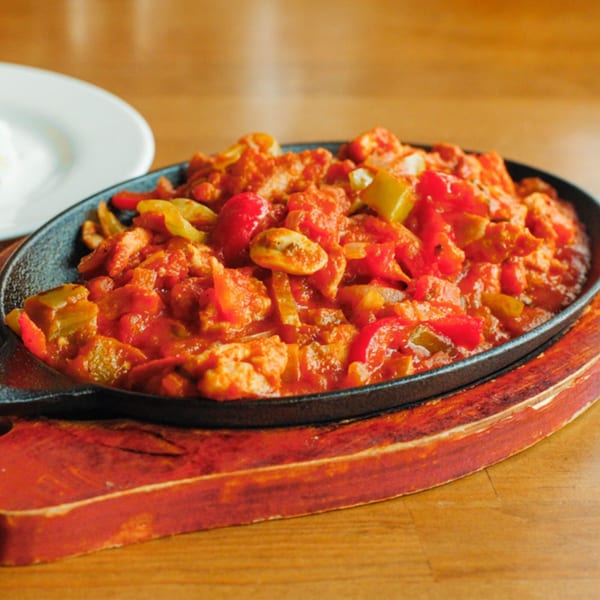 Turkish chicken saute in a cast iron skillet with red and yellow peppers, and tomatoes.