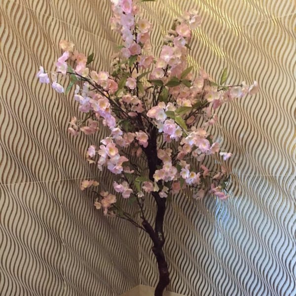 A decorative cherry blossom tree with pink flowers stands against a wavy patterned wall.