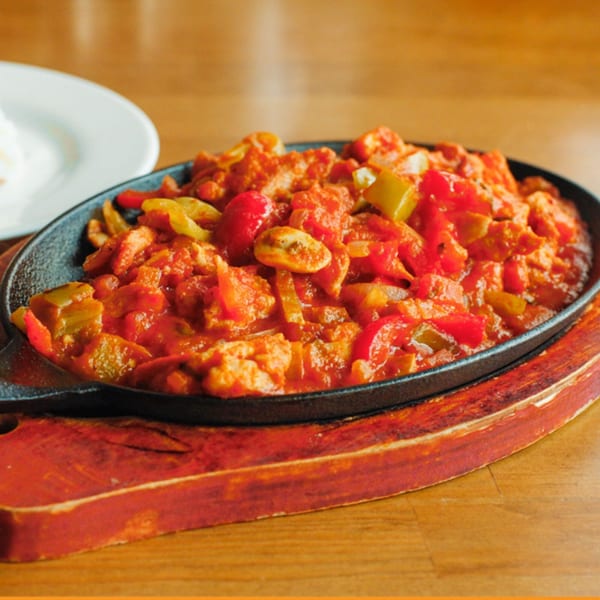 Turkish chicken saute with red and green peppers in a cast iron skillet on a wooden board.