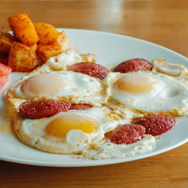Turkish breakfast plate with four fried eggs, sucuk sausage, and roasted potatoes.