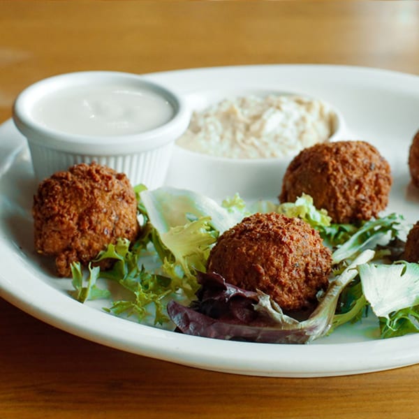 Crispy falafel balls on a bed of fresh lettuce with two dipping sauces on a white plate.