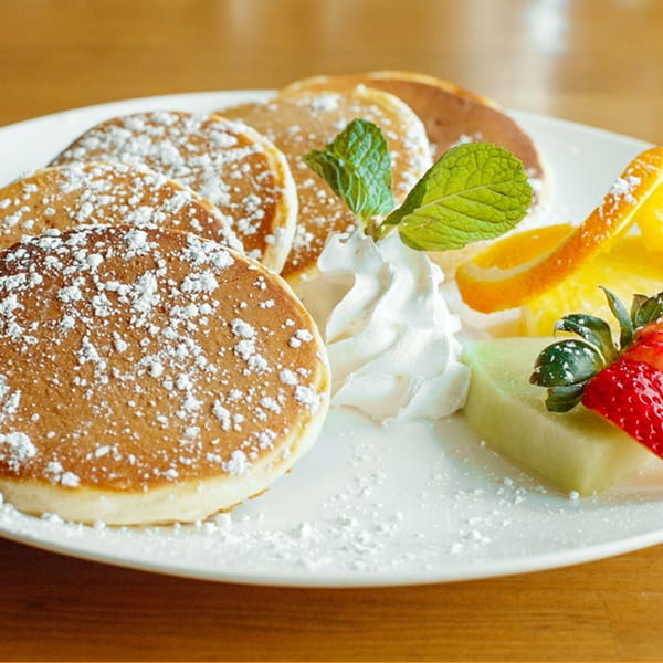Pancakes dusted with powdered sugar, whipped cream, mint, and fresh fruit on a white plate.