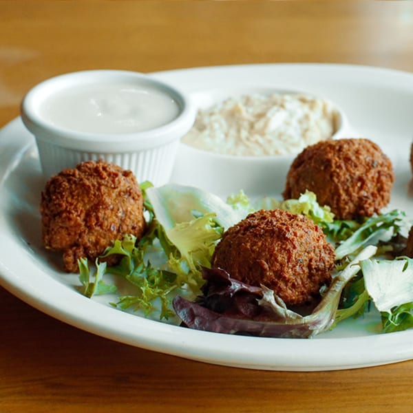 Crispy falafel balls on a bed of fresh lettuce with two dipping sauces on a white plate.