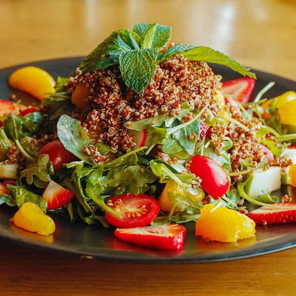 Opera Cafe Lounge's quinoa salad with arugula, strawberries, cherry tomatoes, and mint on a black plate.